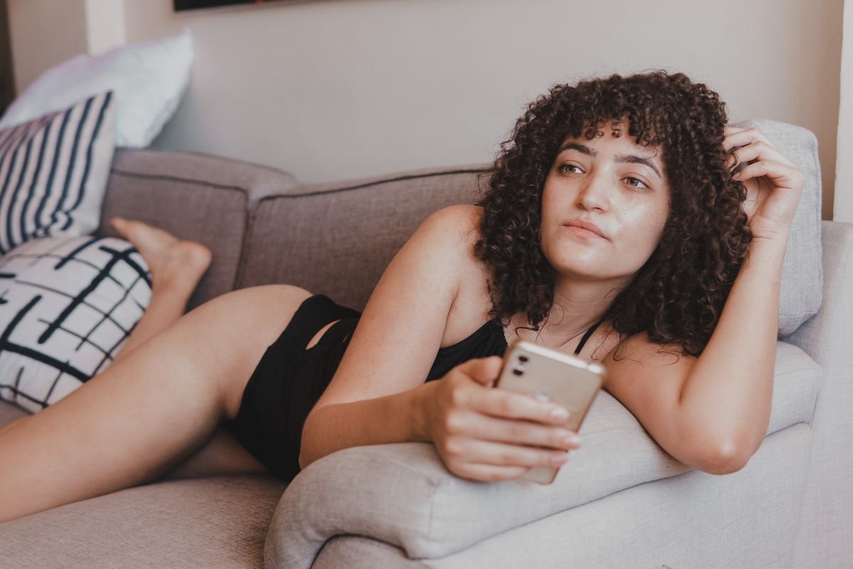 Woman scrolling her phone alone on a sofa while her partner sits nearby