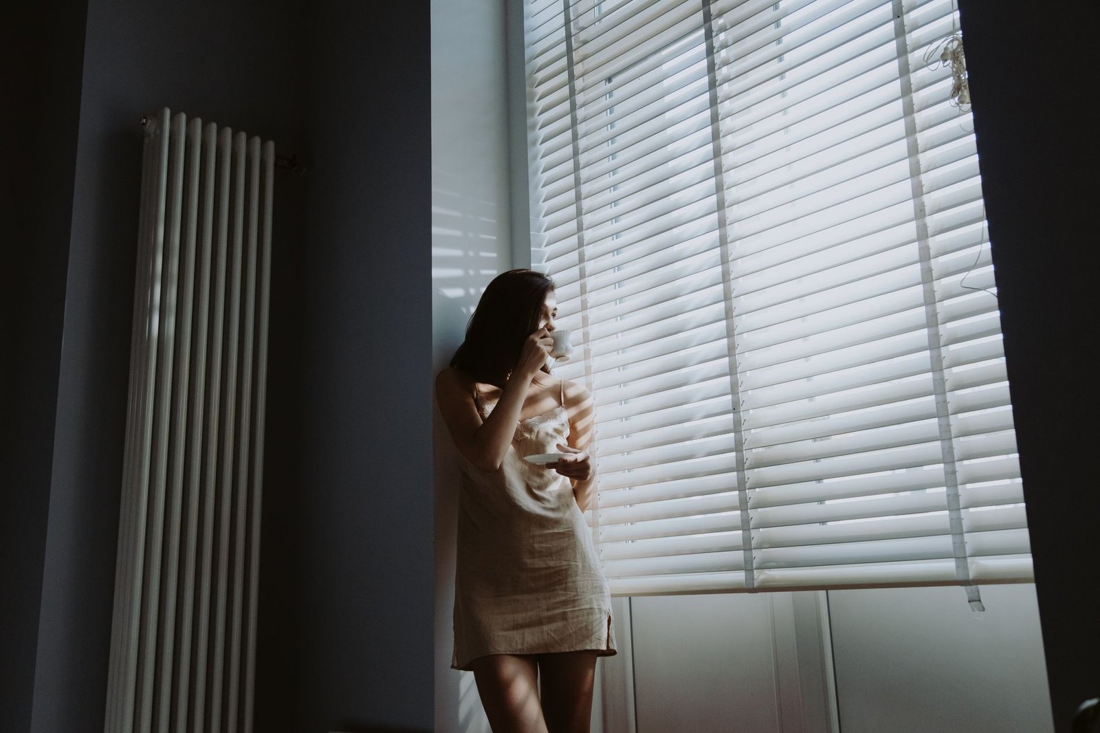Woman holding a coffee mug by a window while missing your partner in a long distance relationship