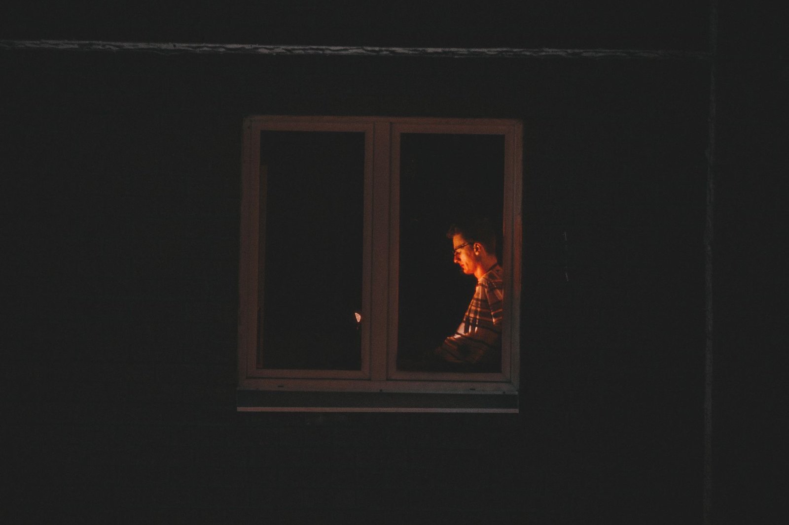 Silhouette of a man working late by a window at night