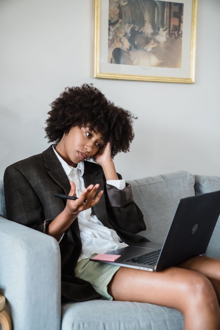 Woman sitting on a couch looking confused at her laptop screen