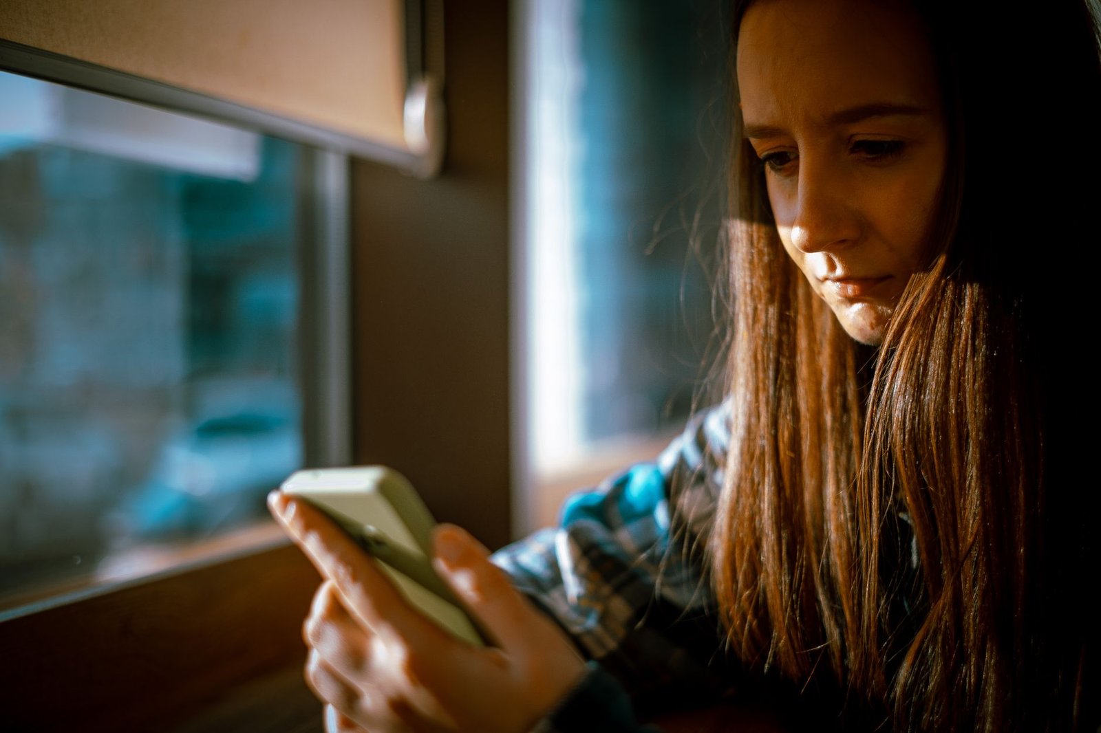 Woman by a window checking her phone for a slow text reply from a guy she is dating