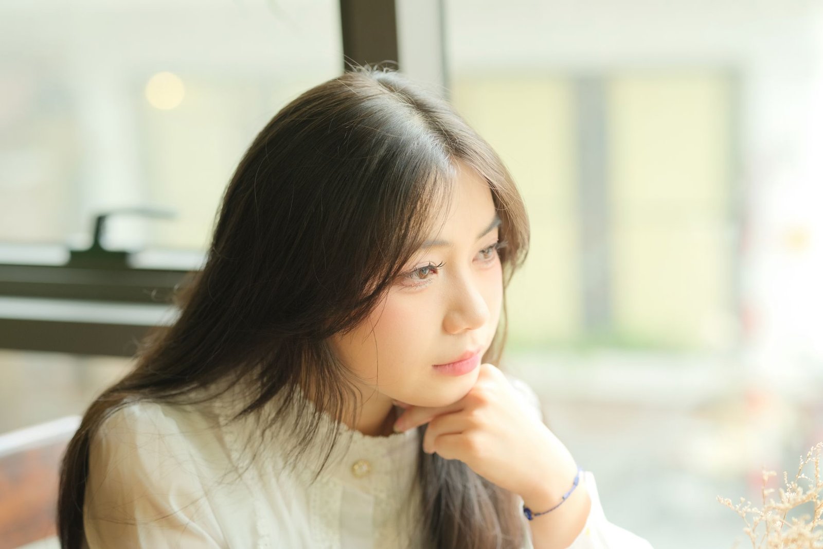 Woman looking out a window thinking about whether to stay friends with her ex after a breakup