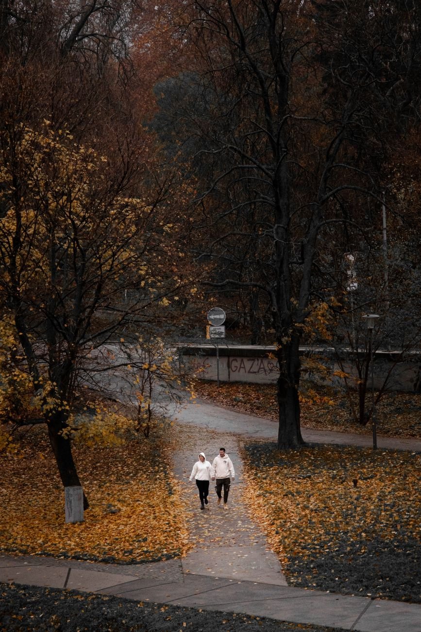 Couple walking on a leaf covered path talking through a disagreement side by side