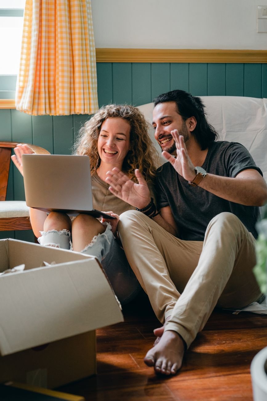 Happy couple sitting near moving boxes chatting on a laptop
