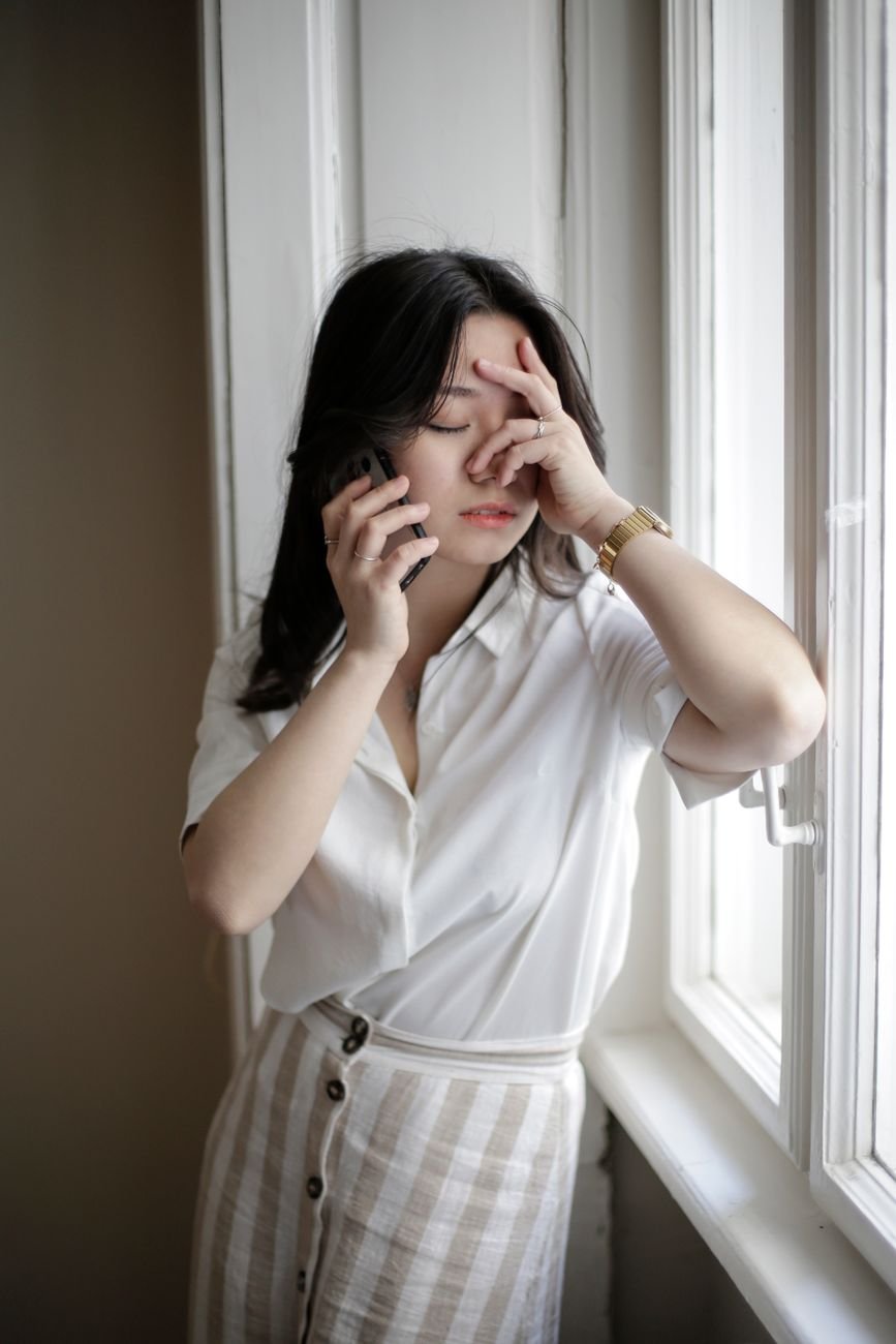 Frustrated woman on the phone by a window, wondering if her long distance partner is losing interest