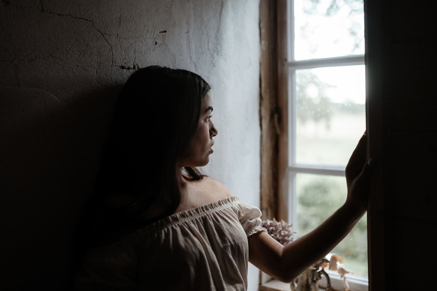 Woman sitting quietly by a window weighing whether long distance love is worth the wait
