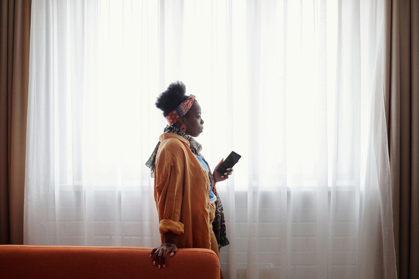 Woman holding her phone by a window thinking about insecurity in a long distance relationship