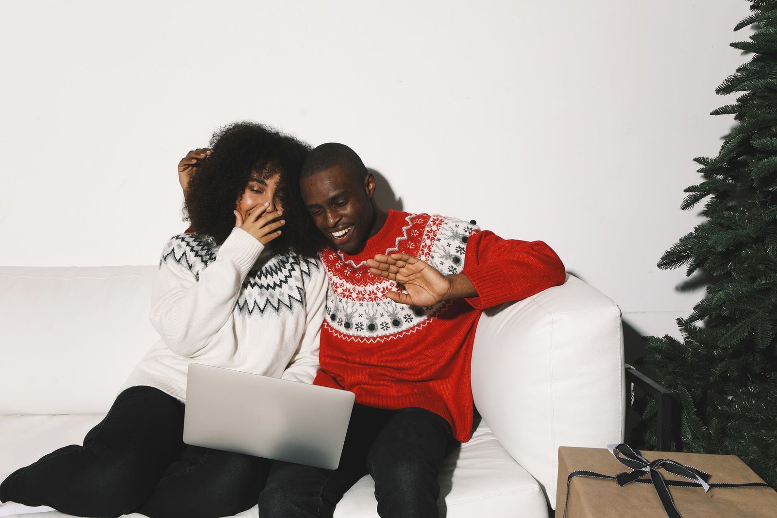 Couple sitting together near a lit Christmas tree during their first holiday season as a couple