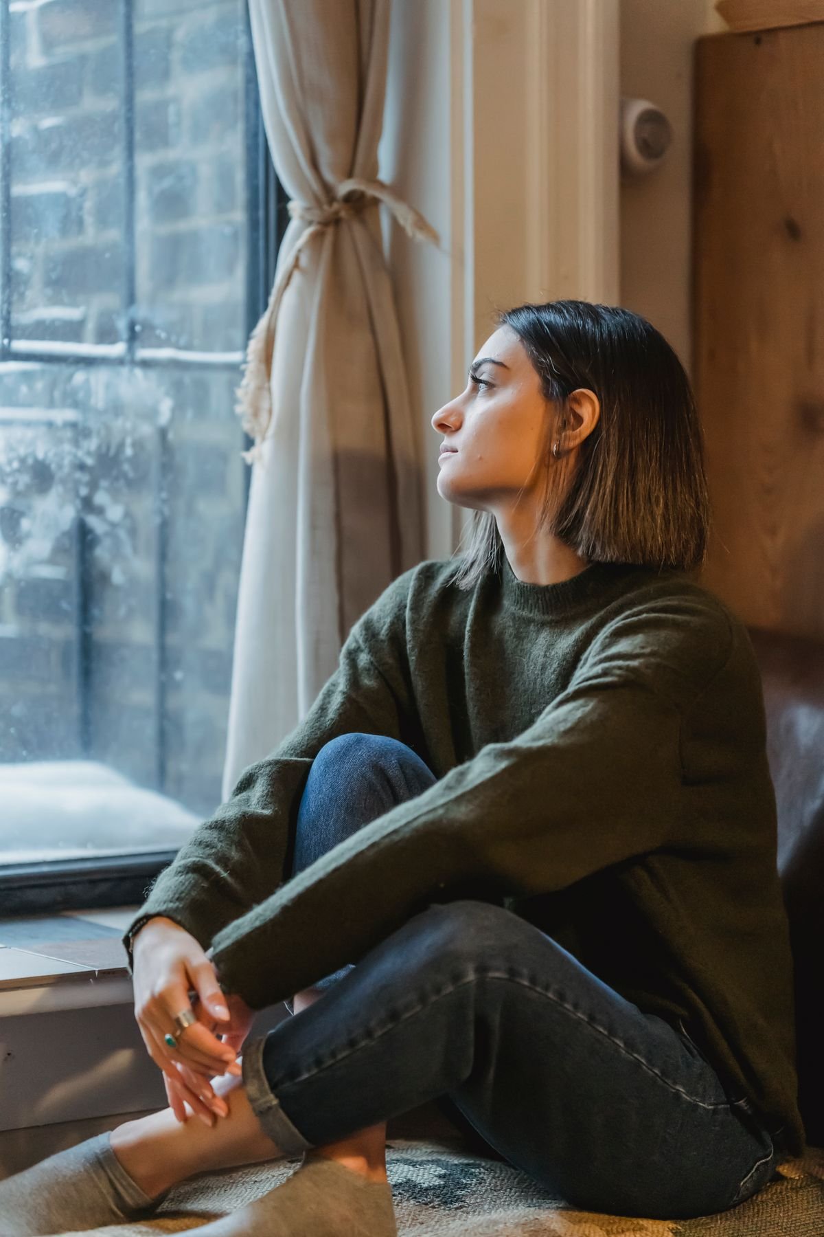 Young woman sitting alone by a window feeling lonely in a long distance relationship