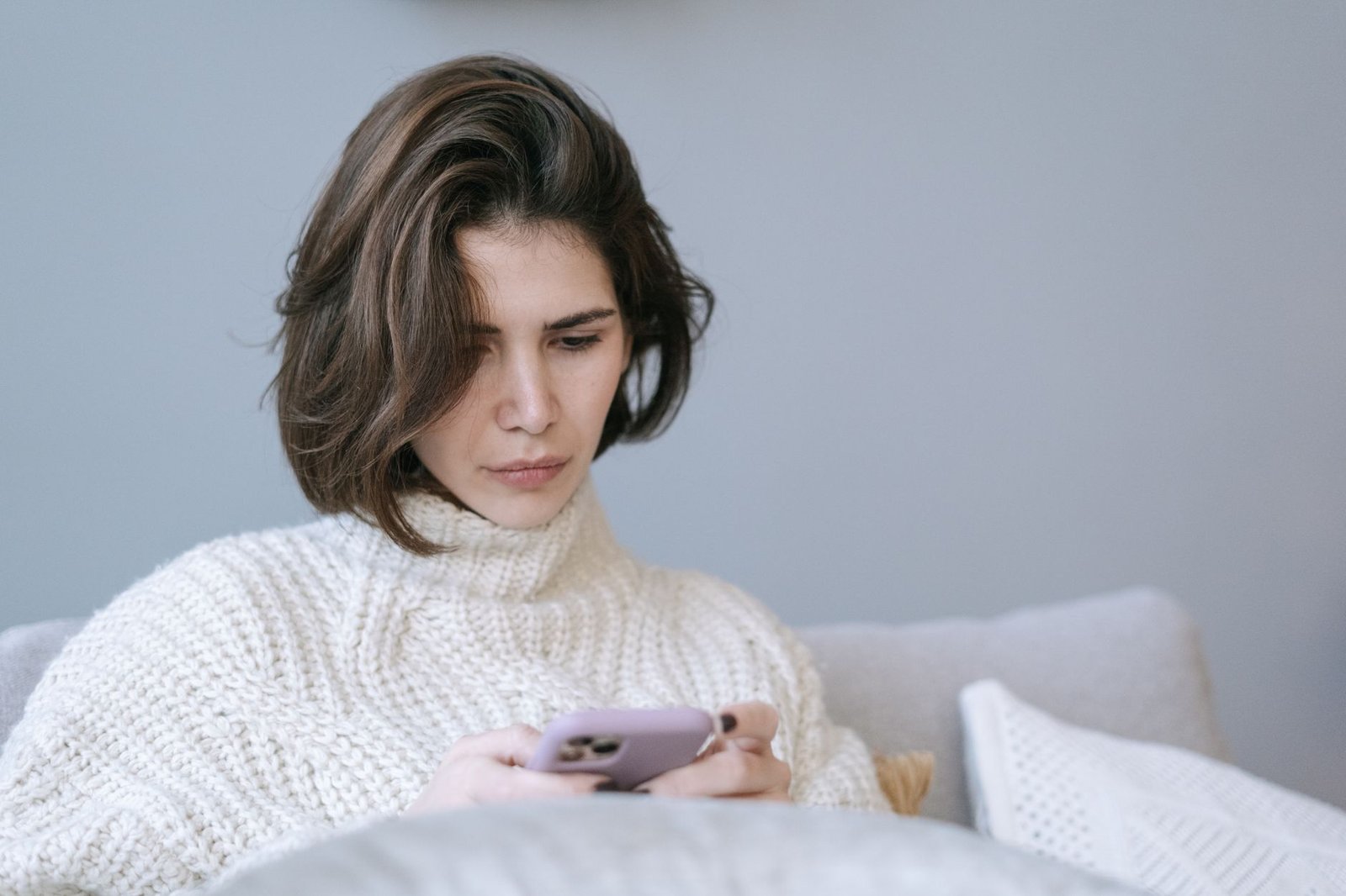 Woman in a cozy sweater looking at her phone with a heavy expression