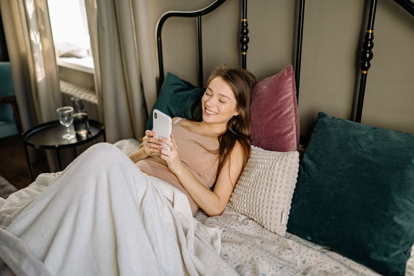 Woman smiling at her phone in bed during a long distance relationship morning check-in