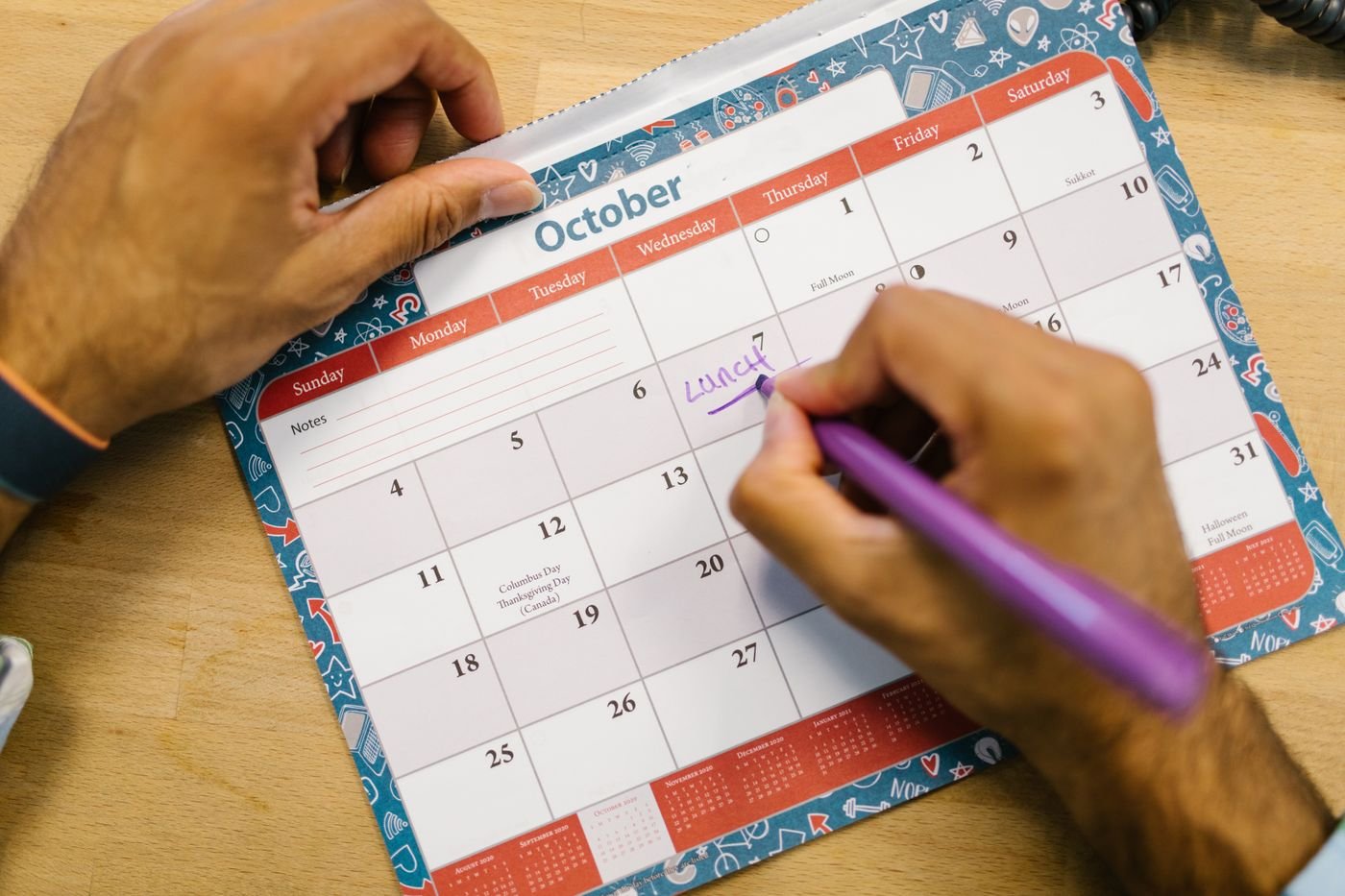 Person writing a reminder on an October calendar to schedule a long distance visit