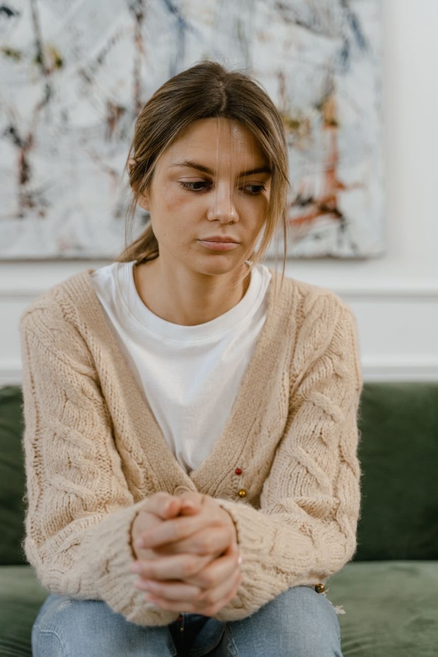 Woman in a cozy sweater sitting alone on a couch replaying a conversation in her head