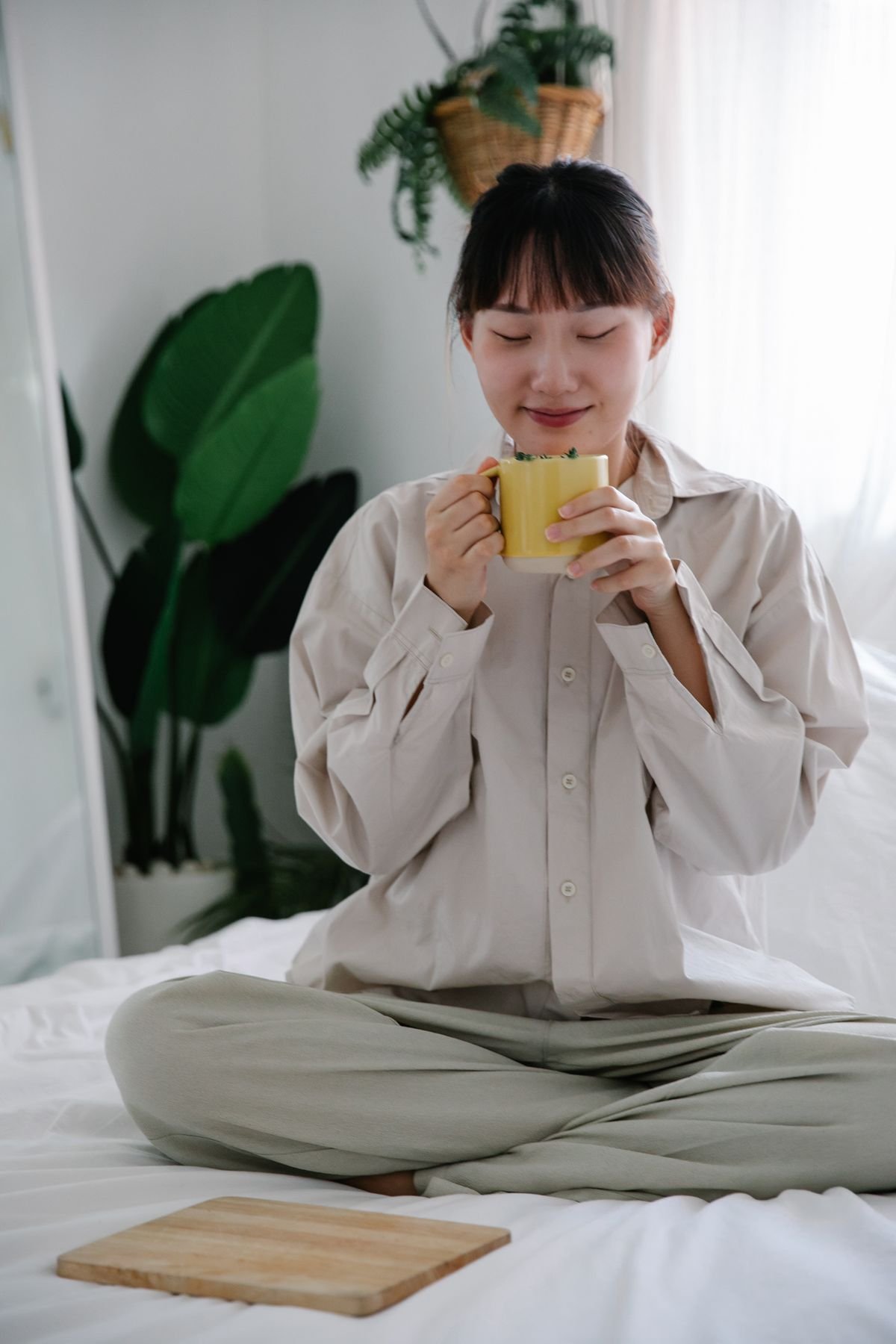 Woman in pajamas sipping tea in bed as part of her long distance self-care routine