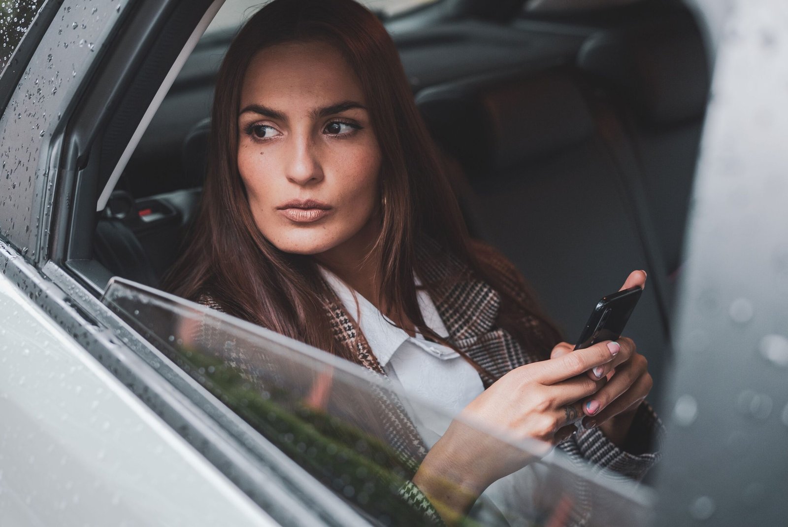 Woman looking out a car window while holding her phone, deep in thought