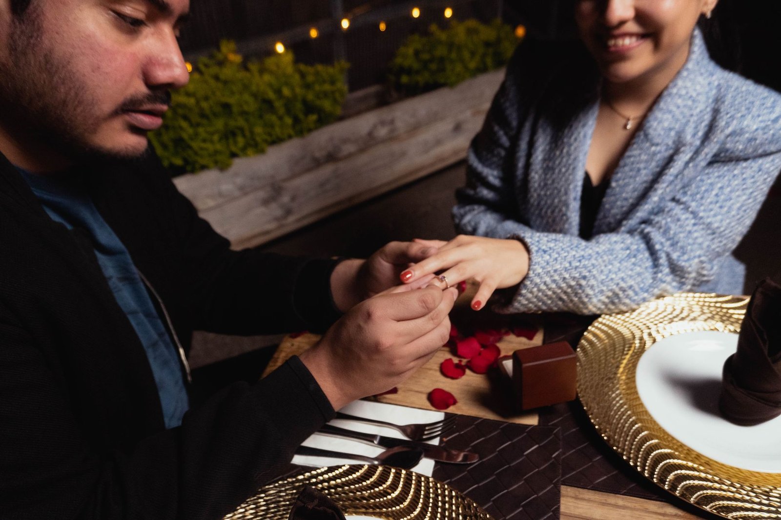 Woman surprised by a birthday proposal at a rooftop dinner with a candle and ring box