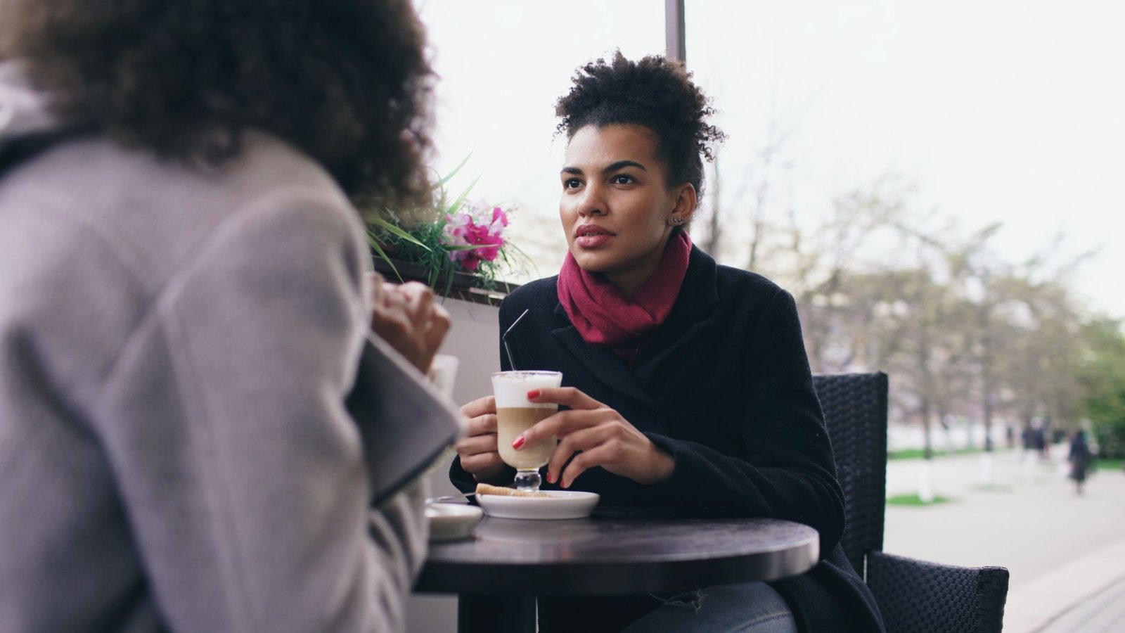 Two friends talking and laughing over coffee at a cafe table