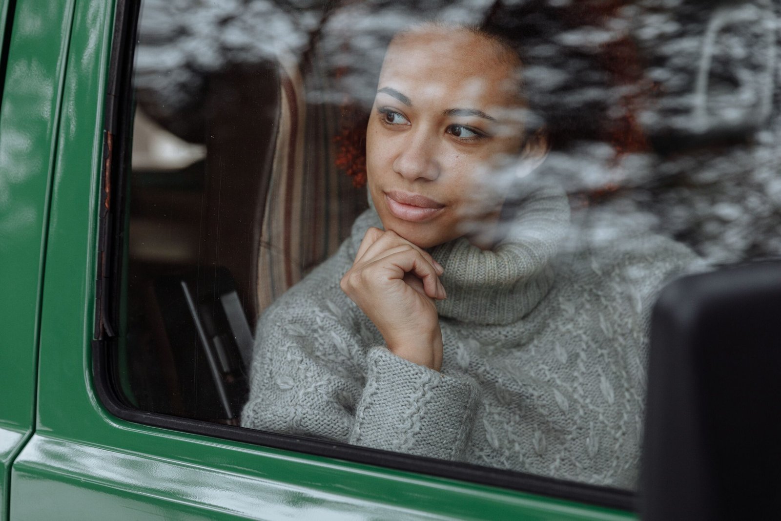 Woman in a sweater gazing thoughtfully out a car window during a drive