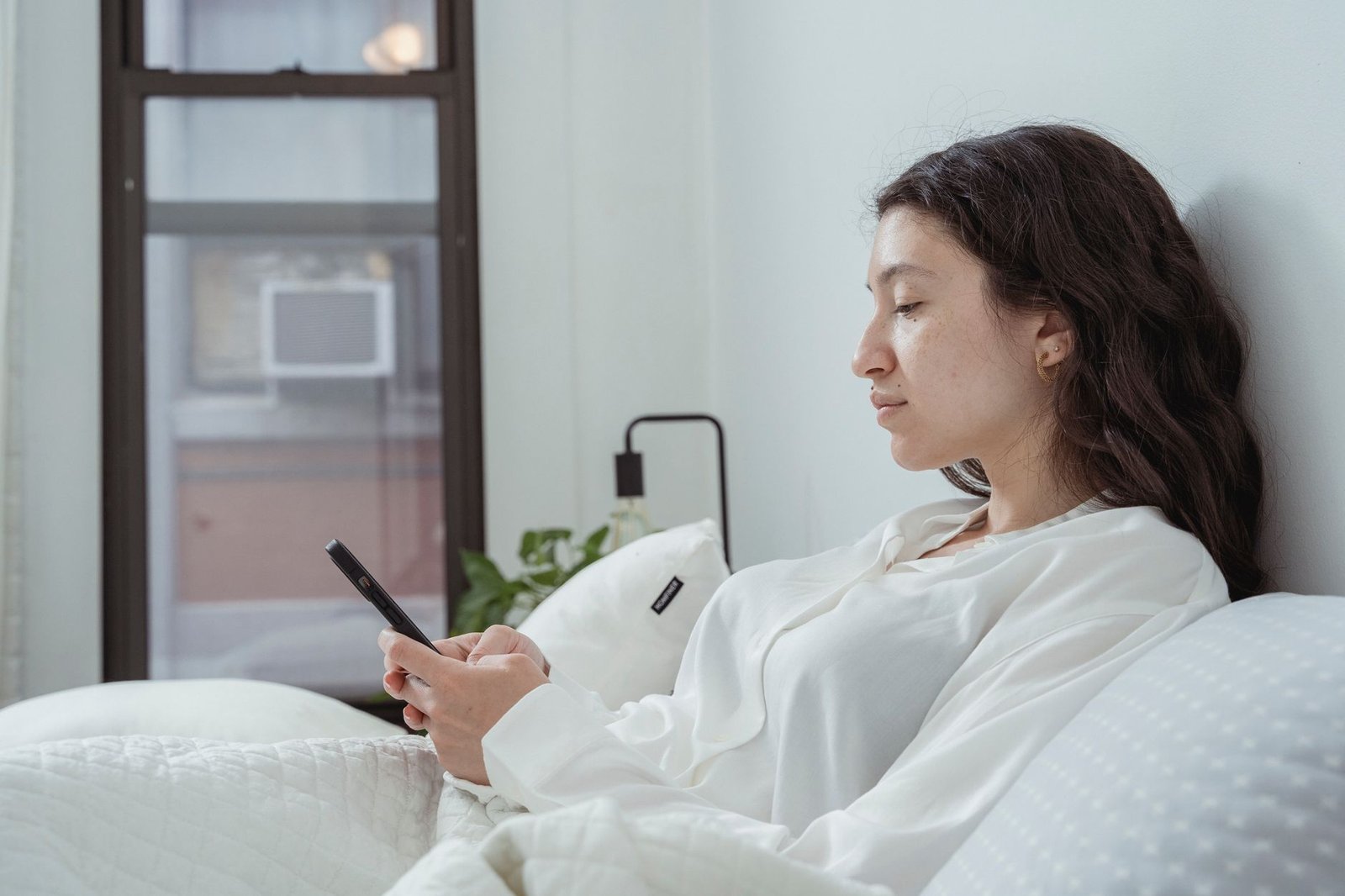 Woman texting on her phone in bed before a first date facetime call